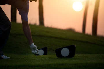 Obraz premium The golfer's hand grips the golf ball and tee presses down at starting point amid sunrise in morning.