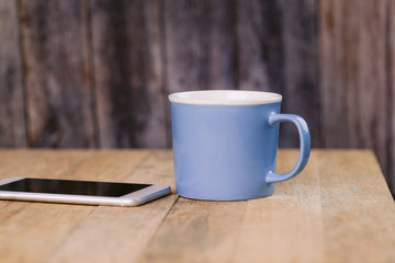 A cellphone on a table with a blue mug
