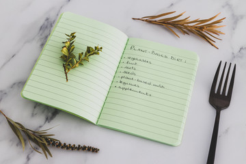 plant-based diet green notebook with food category list with fork and plants