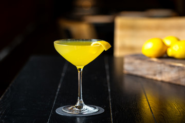 fresh yellow alcohol cocktail with lemon at a restaurant interior, dark background