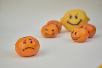 Concept of bullying, discrimination. Group of laughing emoticon faces and one alone look sad and depressed. Lemmons and mandarines. Yellow and Orange fruits.