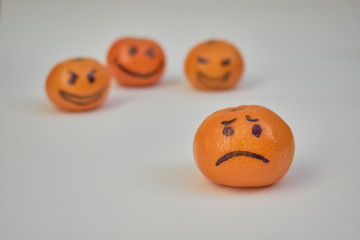 Concept of bullying, discrimination. Group of laughing emoticon faces and one alone look sad and depressed. Lemmons and mandarines. Yellow and Orange fruits.