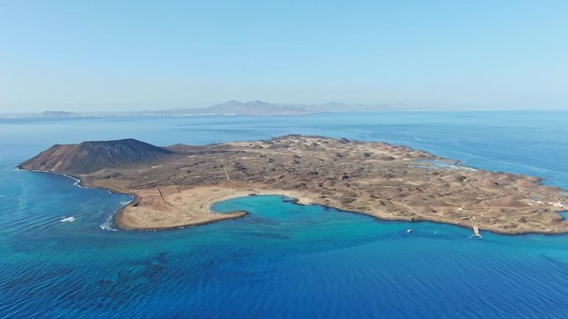 High angle panoramic aerial drone panning footage of Isla de Lobos, a small uninhabited island just 2 kilometres off the coast of Fuerteventura, Canary Islands, Spain. Lanzarote in the background.