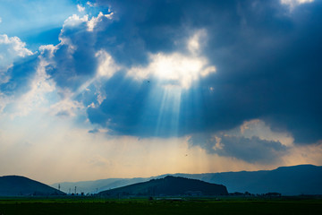 雲の隙間から太陽光のさす阿蘇平野