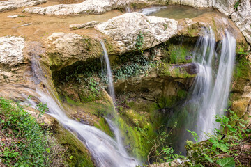 Fototapeta premium Cascades of a small stream flow down the cliffs of light stone.
