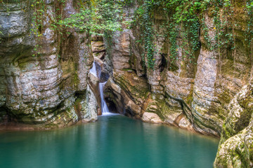 Mountain river and waterfall with clear turquoise water in a stone gorge.