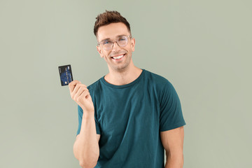 Young man with credit card on color background