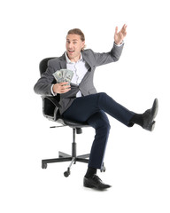 Handsome young businessman with money sitting on chair against white background