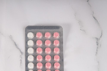 White and pink birth control pills on a marble background