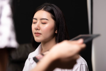 Beautiful young asian woman and professional makeup artists applies eye shadow. Beautiful woman face. Perfect makeup.