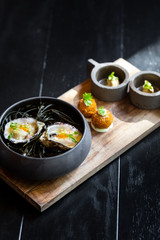 Haute cuisine - noodles with oysters filled by freezy ozone , croutons and yellow sauce on a wooden plate with dark background