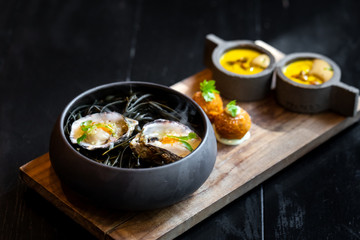 Haute cuisine - noodles with oysters filled by freezy ozone , croutons and yellow sauce on a wooden plate with dark background