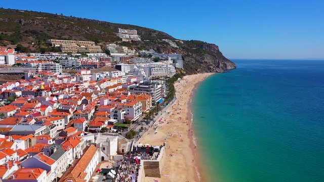 Aerial, reverse, drone shot, overlooking the Sesimbra city and people on the Praia da California beach, on a sunny day, in Lisbon, Portugal