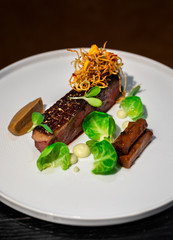 Haute cuisine - a beef steak with greens topping and sauce on a white dish and dark background