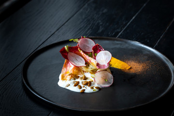 Haute cuisine salad with nuts, sauce and radish on a black dish at dark background