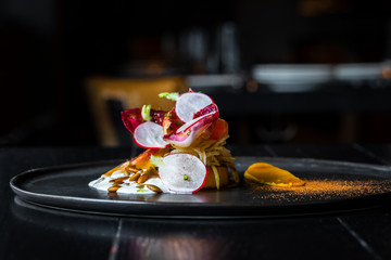 Haute cuisine salad with nuts, sauce and radish on a black dish at dark background