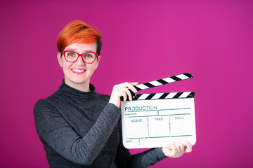 redhead woman holding movie  clapper on pink background