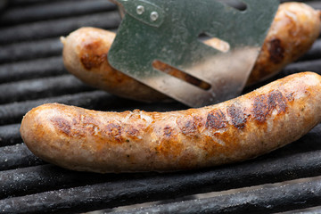 Savory brats cooking on an outdoor iron grill.