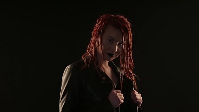 concept dances, parties, advertising leather jackets, styling hair, hairdressing dreadlocks, make-up: dark lipstick. rocker dancing on black background, woman styling red hair