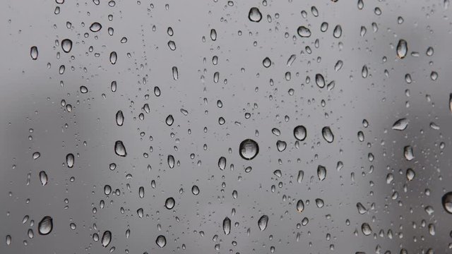Close up video of drops of rain water running down clear glass window. Rain, bad weather concept. Blurred background. Bokeh/selective focus. Filmed in Panama City in Panama during the rainy season. 4K