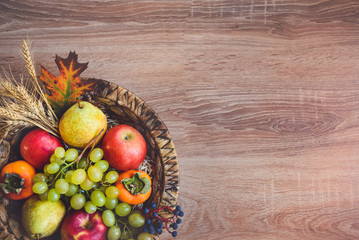 Top view of various colorful autumn fruits in a wicker basket over wooden table. Copy space.