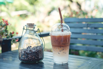 Refreshing iced coffee and coffee bean in bottle for decoration on wooden table in a garden cafe on a beautiful summer day in Thailand with copyspace - Soft focus