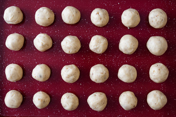 Raw shaped Russian Tea Cake cookies on a red non-stick baking sheet, ready to bake