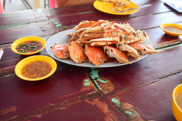 Steamed Blue Crab cooked in a white plate and a spicy sauce in a cup on red wooden table, Seafood and Local cuisine in Thailand
