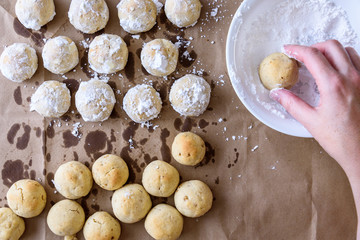 Fresh baked Russian Tea Cake cookies cooking on brown paper, woman’s hand, bowl of powdered sugar ready to roll cookies in