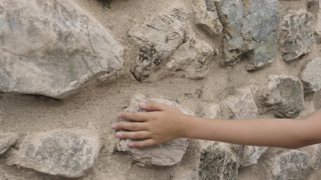 Cropped shot of human hand touching stone wall. Close-up partial view of child walking and touching ancient wall with palm at sunny summer day
