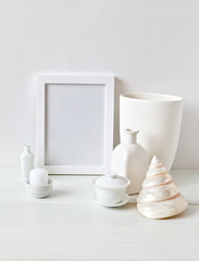 A minimalist still life with an empty frame, a sea shell, a vase, a bottle and a candle on a white background