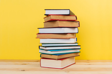 Simple composition of many hardback books, raw of books on wooden table and pastel yellow background