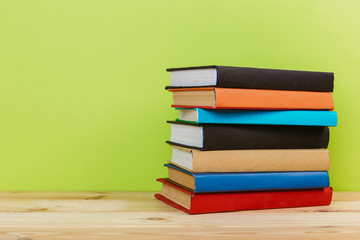 Simple composition of many hardback books, raw of books on wooden table and light green background