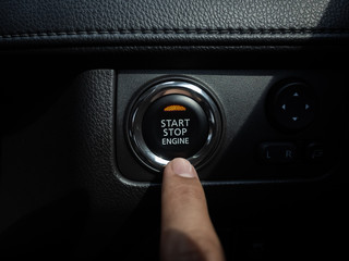 Start-Stop engine button with orange light on black car console background.