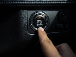 Start-Stop engine button with orange light on black car console background.