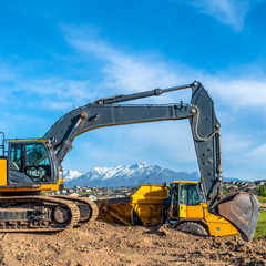 Square Excavator with metal arm and bucket and continuous tracks at a construction site