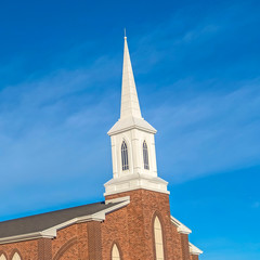 Square Exterior of a church with red brick wall arched windows and white steeple