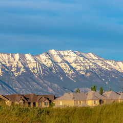 Square Mountain with snowy peak towering over family houses with blue sky overhead