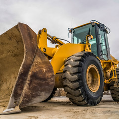 Square Side view of a yellow bulldozer with dirty metal bucket and black rubber wheels © Jason