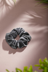 Object photo of a grey velvet scrunchie. The scrunchie is lying on a beige background. There are...