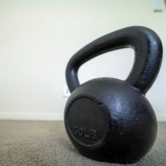 Naklejka na ściany i meble Square frame Focus on a heavy kettlebell inside a room with carpeted floor and white wall