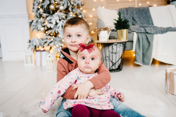 Fototapeta premium Kids sit on floor near Christmas tree. Happy New Year and Merry Christmas. Christmas decorated interior. The concept of family winter holiday.