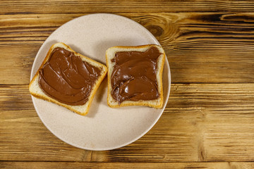 Two slices of bread with delicious chocolate hazelnut spread on wooden table. Top view