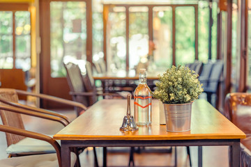 A small bell for calling the waiter and artificial flowers in an aluminum pot and drinking water bottle placed on a table in a coffee shop