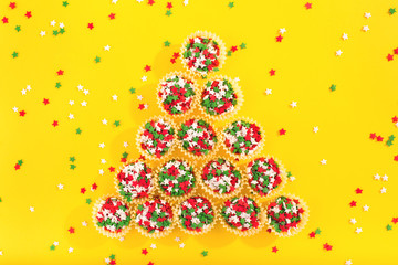Colorful sprinkles on a yellow background making a shape of a Christmas tree. Flat lay style. Top view.