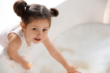 Cute little girl near tub in bathroom. Space for text