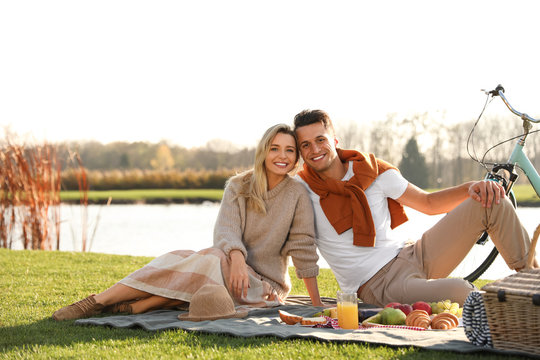 Happy young couple having picnic near lake on sunny day