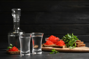 Cold Russian vodka and sandwiches with red caviar on black table