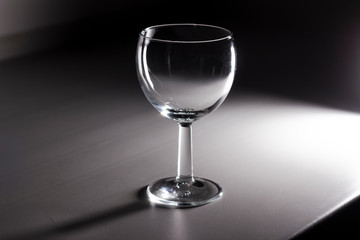 Empty wine glass on a white table in a dark room.