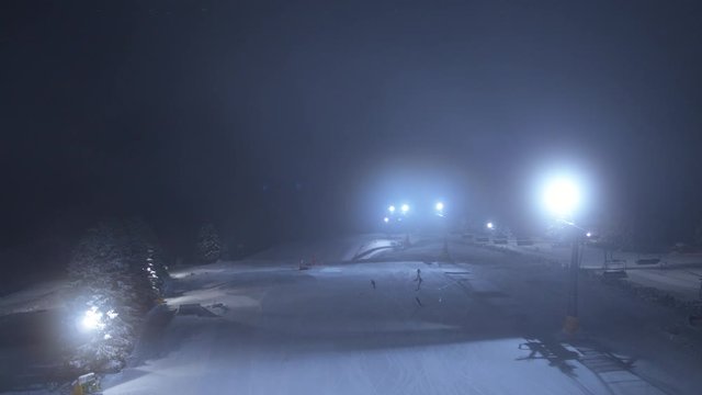 Drohnenaufnahme von einem Flutlicht beleuchteten Skigebiet, mit Skilift in einem Schneebedeckten Wald